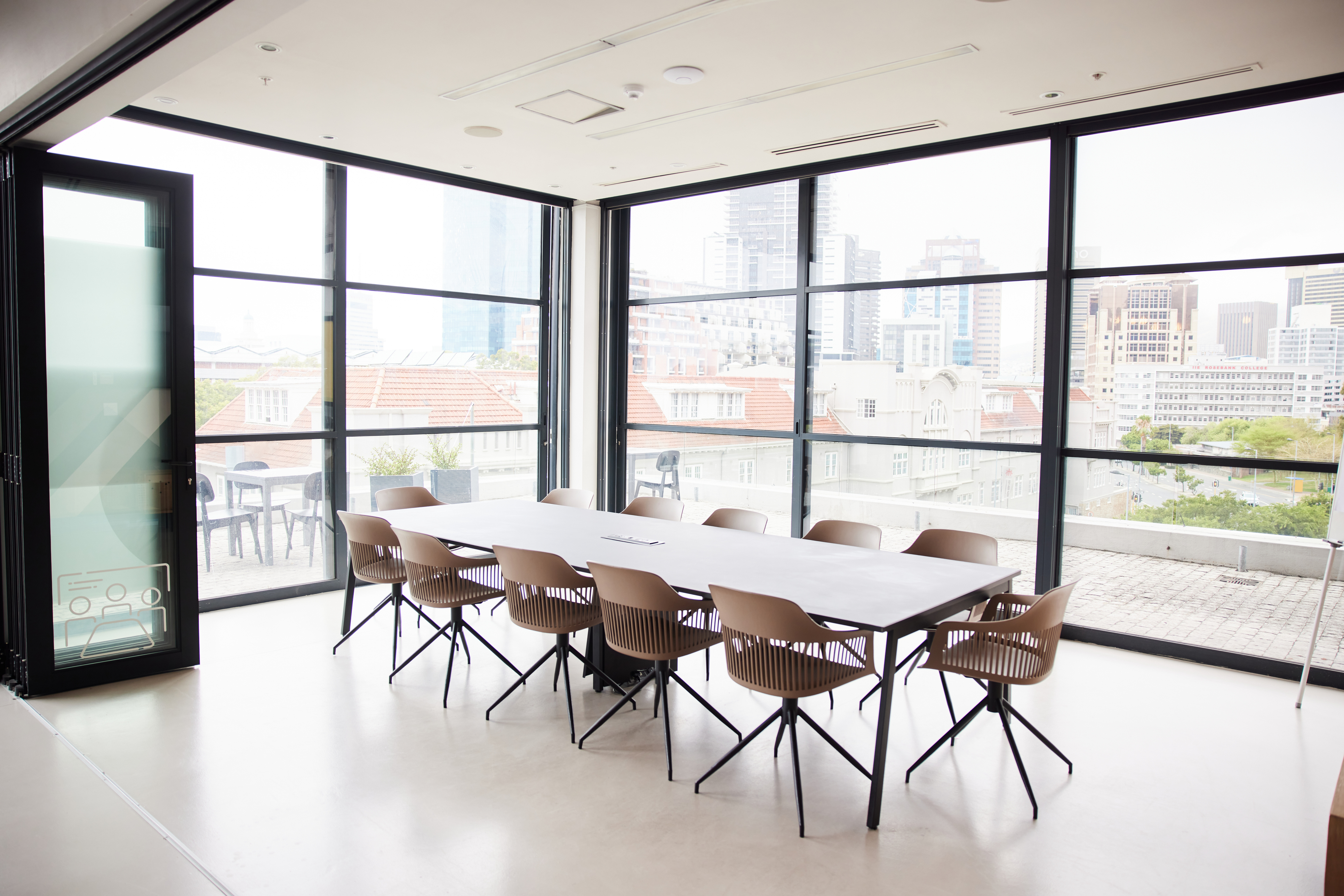 Conference table and chairs sitting in an empty glass-walled boardroom in a modern office space